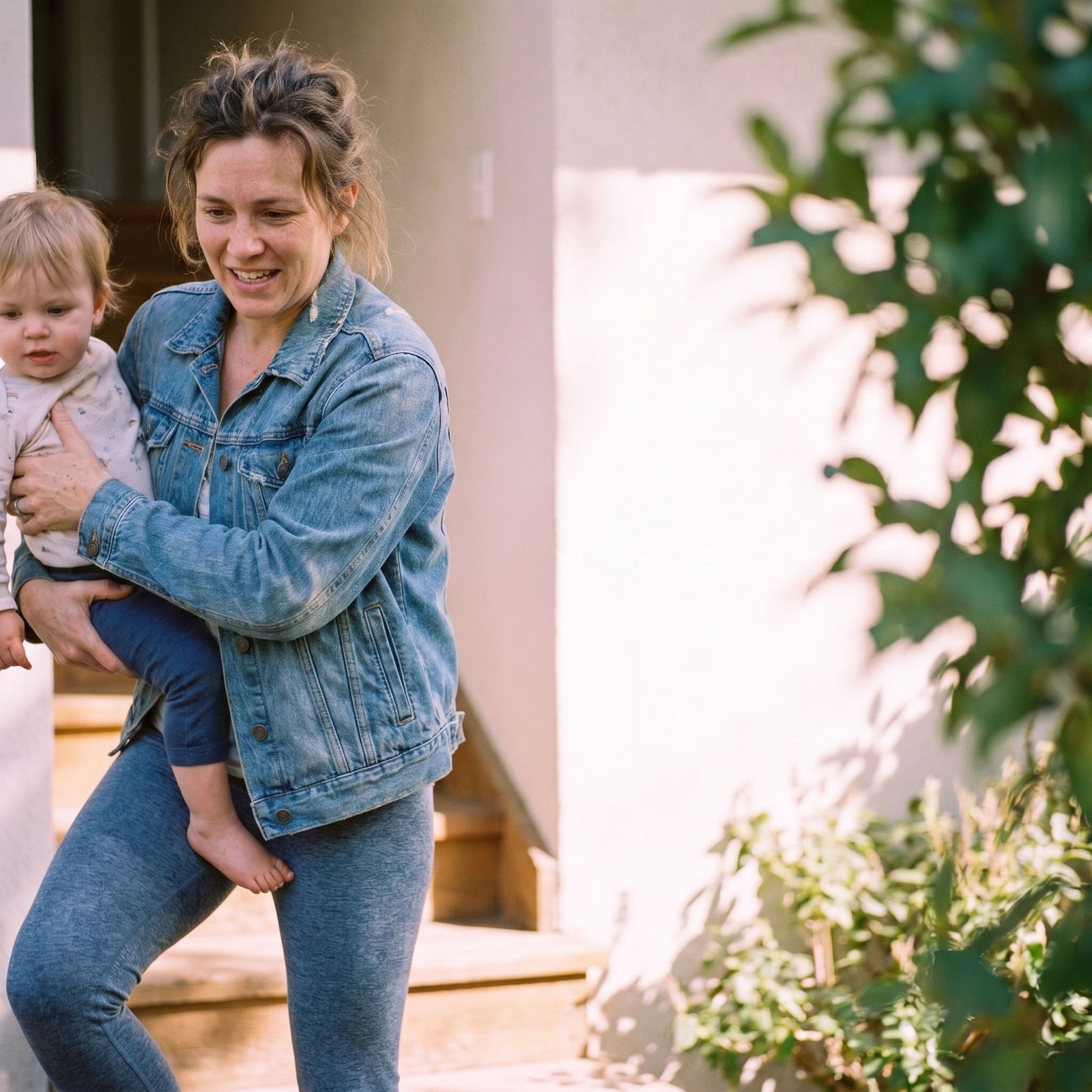 Mom smiling as she carries her toddler up the front steps